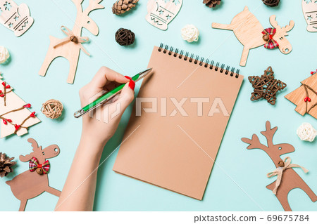 Top view of female hand making some notes in noteebok on blue background. New Year decorations and toys. Christmas time concept Top view of female hand making some notes in noteebok on blue background. New Year decorations and toys. Christmas time concept 69675784