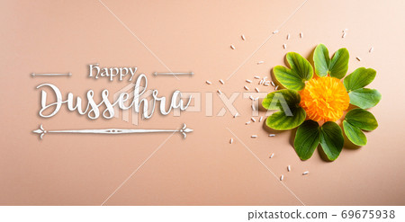 Happy Dussehra. Yellow flowers, green leaf and rice on orange pastel background. Dussehra Indian Festival concept. 69675938
