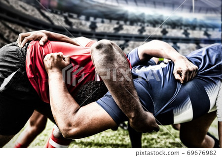 Digital composite image of two rugby players tackling each other in sports stadium Digital composite image of two rugby players tackling each other in sports stadium 69676982