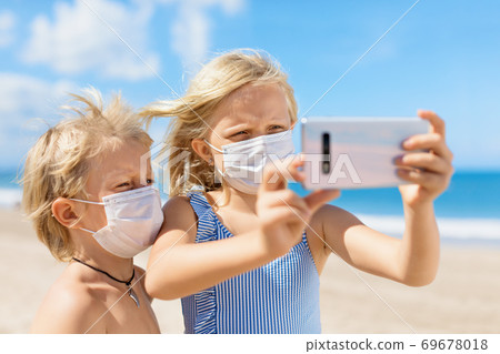 Funny kids in face masks taking selfie photo on beach Funny kids in face masks taking selfie photo on beach 69678018