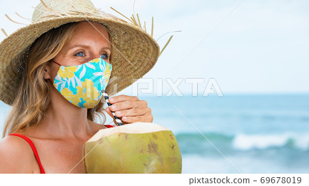 Woman wearing face mask drinking young coconut on tropical beach Woman wearing face mask drinking young coconut on tropical beach 69678019