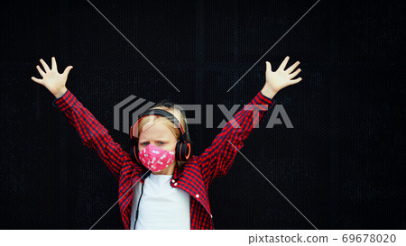 Young positive child in face mask listening music in headphones Young positive child in face mask listening music in headphones 69678020