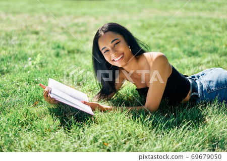 Pretty afro american woman reading book lying in grass in park Pretty afro american woman reading book lying in grass in park 69679050
