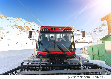 Red modern snowcat ratrack with snowplow snow grooming machine preparing ski slope piste hill at alpine skiing winter resort Ischgl in Austria. Heavy machinery mountain equipment track vehicle 69679695