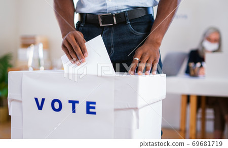 Unrecognizable african-american man putting his vote in the ballot box, usa elections and coronavirus. Unrecognizable african-american man putting his vote in the ballot box, usa elections and coronavirus. 69681719