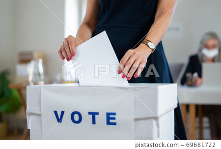 Unrecognizable woman putting her vote in the ballot box, usa and coronavirus elections. Unrecognizable woman putting her vote in the ballot box, usa and coronavirus elections. 69681722