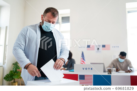 Mature man putting his vote in the ballot box, usa elections and coronavirus. 69681829