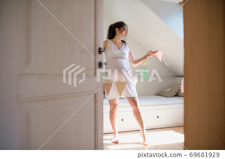 Pregnant woman indoors at home, decorating bedroom for newborn baby. Pregnant woman indoors at home, decorating bedroom for newborn baby. 69681929
