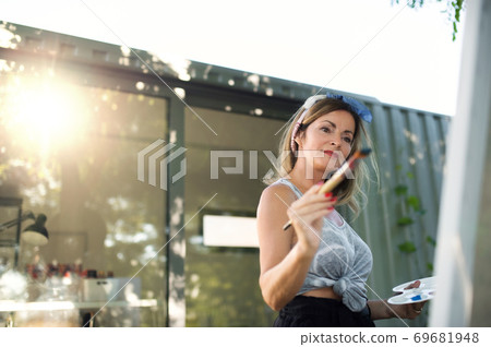 Portrait of mature woman with pallete painting outdoors in garden. 69681948