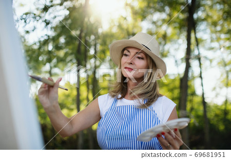 Portrait of mature woman with pallete painting outdoors in garden. Portrait of mature woman with pallete painting outdoors in garden. 69681951
