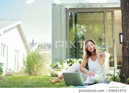 Mature woman working in home office outdoors in garden, using smartphone. 69681974