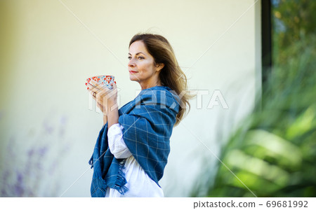 Mature woman with cup of tea resting outdoors in backyard. Mature woman with cup of tea resting outdoors in backyard. 69681992