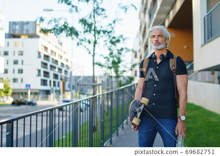 Portrait of mature man with skateboard outdoors in city, going back to work. 69682751