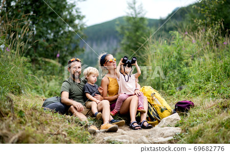 Family with small children hiking outdoors in summer nature, sitting and resting. 69682776