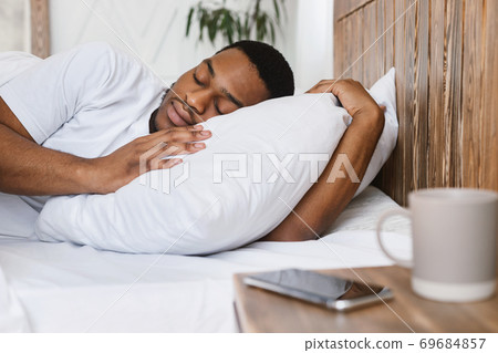 African Guy Sleeping Through Alarm-Clock Lying In Bed At Home African Guy Sleeping Through Alarm-Clock Lying In Bed At Home 69684857