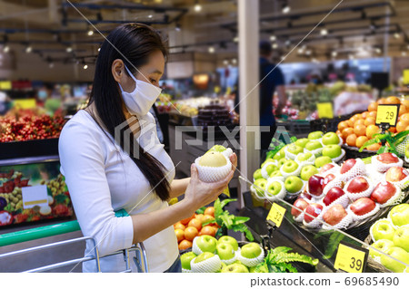 Asian woman wearing protective face mask push and hold shopping cart in supermarket department store. Girl, looking grocery to buy  some food. New normal after covid-19. Family concept. 69685490