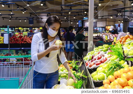 Asian woman wearing protective face mask push and hold shopping cart in supermarket department store. Girl, looking grocery to buy  some food. New normal after covid-19. Family concept. 69685491