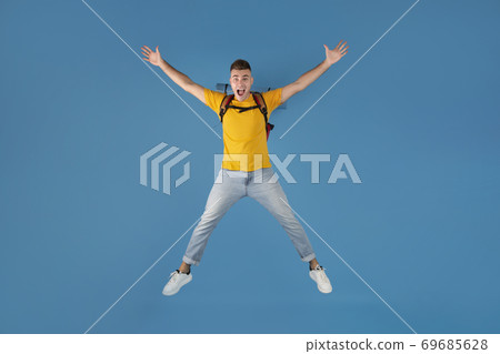 Handsome millennial guy with backpack jumping in excitement over blue studio background 69685628