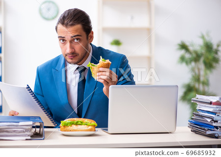 Young male employee having breakfast at workplace Young male employee having breakfast at workplace 69685932