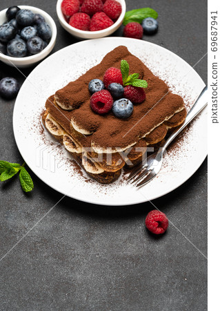 portion of Classic tiramisu dessert with raspberries and blueberries on dark concrete background 69687941