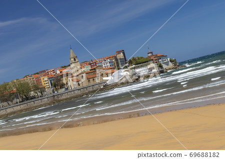 Beautiful seagull flies in stormy weather against the backdrop of an ancient city and a sandy beach with ocean surf. Blue clear sky. In search of shelter from the wind and food. Scenic view 69688182