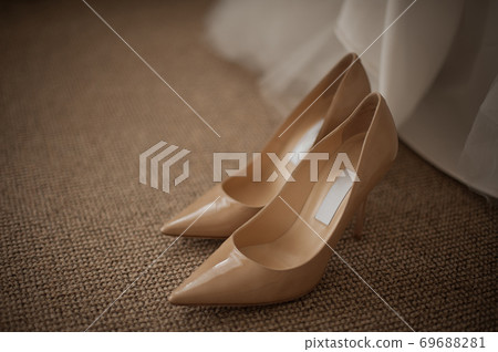 Beige shoes for the bride stand on the floor near the wedding dress Beige shoes for the bride stand on the floor near the wedding dress 69688281