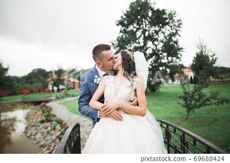 Romantic, fairytale, happy newlywed couple hugging and kissing in a park, trees in background Romantic, fairytale, happy newlywed couple hugging and kissing in a park, trees in background 69688424