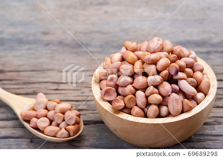Raw Groundnuts in wooden bowl on wood plate Raw Groundnuts in wooden bowl on wood plate 69689298