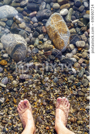 feet on the beach on the shore of the beach with rocks pebbles. vertical photo 69690714