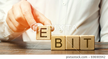 Businessman puts wooden blocks with word Ebit - earnings before interest and taxes. Measure of a firm's profit that includes all incomes and expenses. Operating income. Business and finance concept 69690942