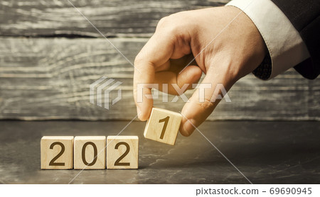 Man puts wooden blocks 2021. The concept of the beginning of the new year. New goals. Next decade. Trends and changes in the world. Build plans and planning. Time report Man puts wooden blocks 2021. The concept of the beginning of the new year. New goals. Next decade. Trends and changes in the world. Build plans and planning. Time report 69690945