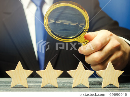 A man holds a magnifying glass over four stars. The evaluation of visitors. Quality level, good service. Best customer rating. Feedback. Rating of hotels and restaurants. Selective focus 69690946