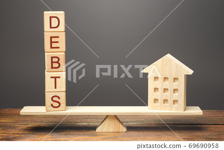 Wooden blocks with the word Debts and a miniature house on the scales. The concept of paying off debts for real estate and housing. Mortgage, loan. Rent apartment Wooden blocks with the word Debts and a miniature house on the scales. The concept of paying off debts for real estate and housing. Mortgage, loan. Rent apartment 69690958