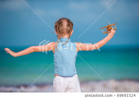 Happy little girl with toy airplane in hands on white sandy beach. Happy little girl with toy airplane in hands on white sandy beach. 69691524