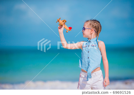 Happy little girl with toy airplane in hands on white sandy beach. Happy little girl with toy airplane in hands on white sandy beach. 69691526