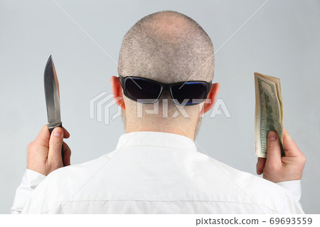 man stands with his back with money and a knife in his hands. man stands with his back with money and a knife in his hands. 69693559