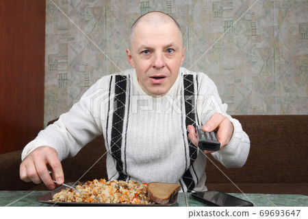 the man eats rice pilaf and stares of TV program the man eats rice pilaf and stares of TV program 69693647