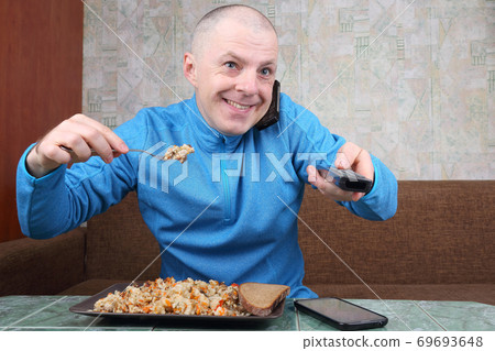the man eats rice pilaf and stares of TV program the man eats rice pilaf and stares of TV program 69693648