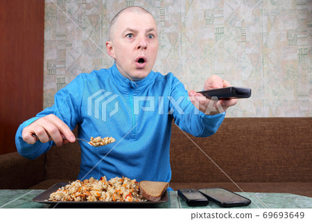 the man eats rice pilaf and stares of TV program the man eats rice pilaf and stares of TV program 69693649