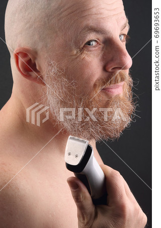 Bearded man with trimmer to adjust beard in hand 69693653