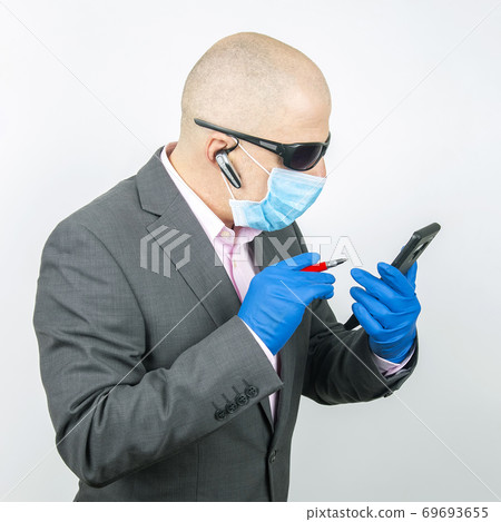 Successful businessman in a protective mask and gloves works on a smartphone during quarantine Successful businessman in a protective mask and gloves works on a smartphone during quarantine 69693655