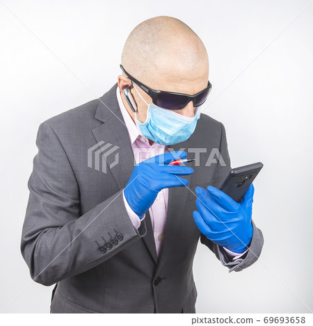 businessman in a protective mask and gloves works on a smartphone during quarantine businessman in a protective mask and gloves works on a smartphone during quarantine 69693658