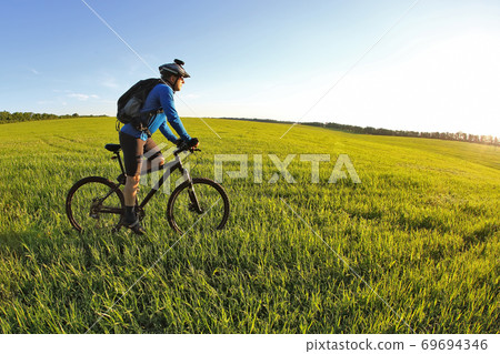 cyclist rides a bicycle on the green field towards the sun 69694346