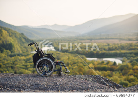 Empty wheelchair on the mountains at sunset. Concept of travel of people with disabilities. 69694377