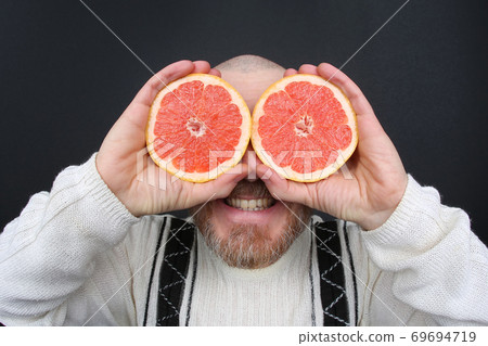 smiling bearded man with a cut grapefruit in his hands smiling bearded man with a cut grapefruit in his hands 69694719