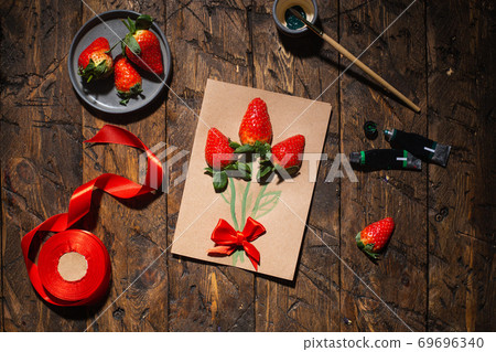 Gift card with live strawberries. On the table are satin ribbon, paintbrush and tubes of paint. Top Gift card with live strawberries. On the table are satin ribbon, paintbrush and tubes of paint. Top 69696340