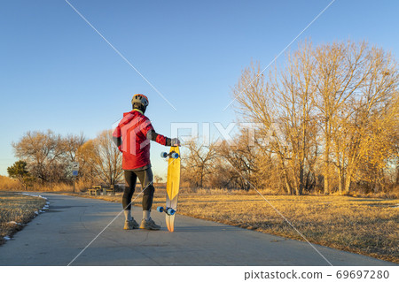 senior man with a cruising longboard on a bike trail 69697280