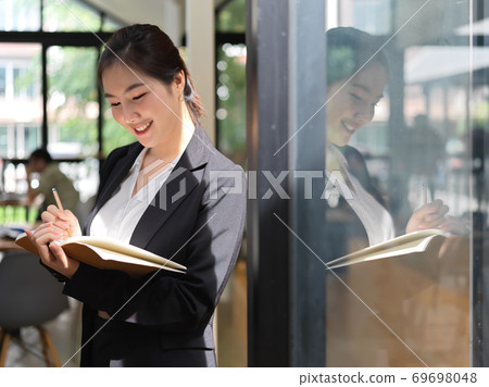 Businesswoman taking note on schedule book in glass partition office room 69698048