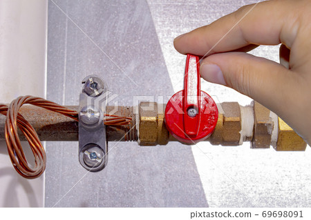 A person turning on off a natural gas red tap. 69698091
