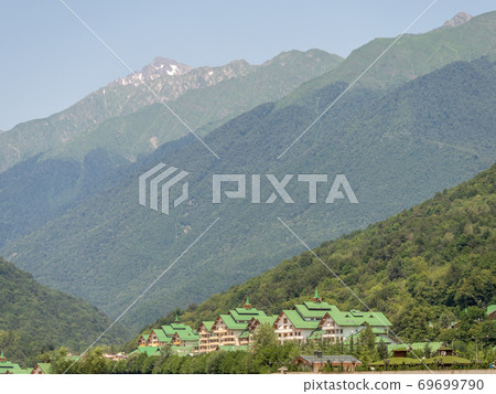 Hotel complex at the foot of high green mountains with snowy peaks 69699790
